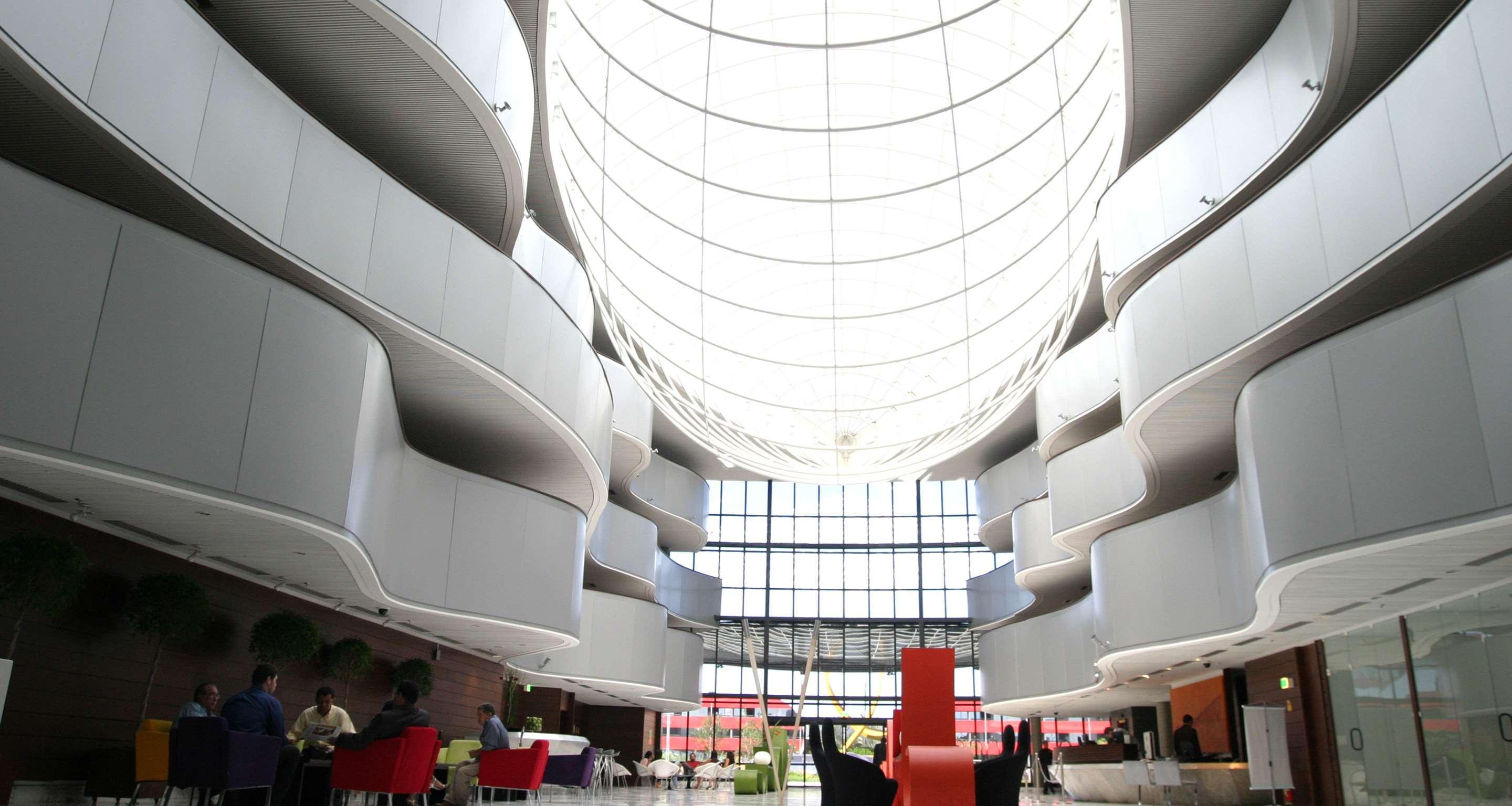 Hotel Royal Tulip Brasilia Alvorada Exterior foto The photo depicts a modern interior space characterized by sleek, curvilinear architecture. The ceiling features a large, dome-like skylight that allows natural light to flood the area. The walls display a minimalist design with smooth, white surface