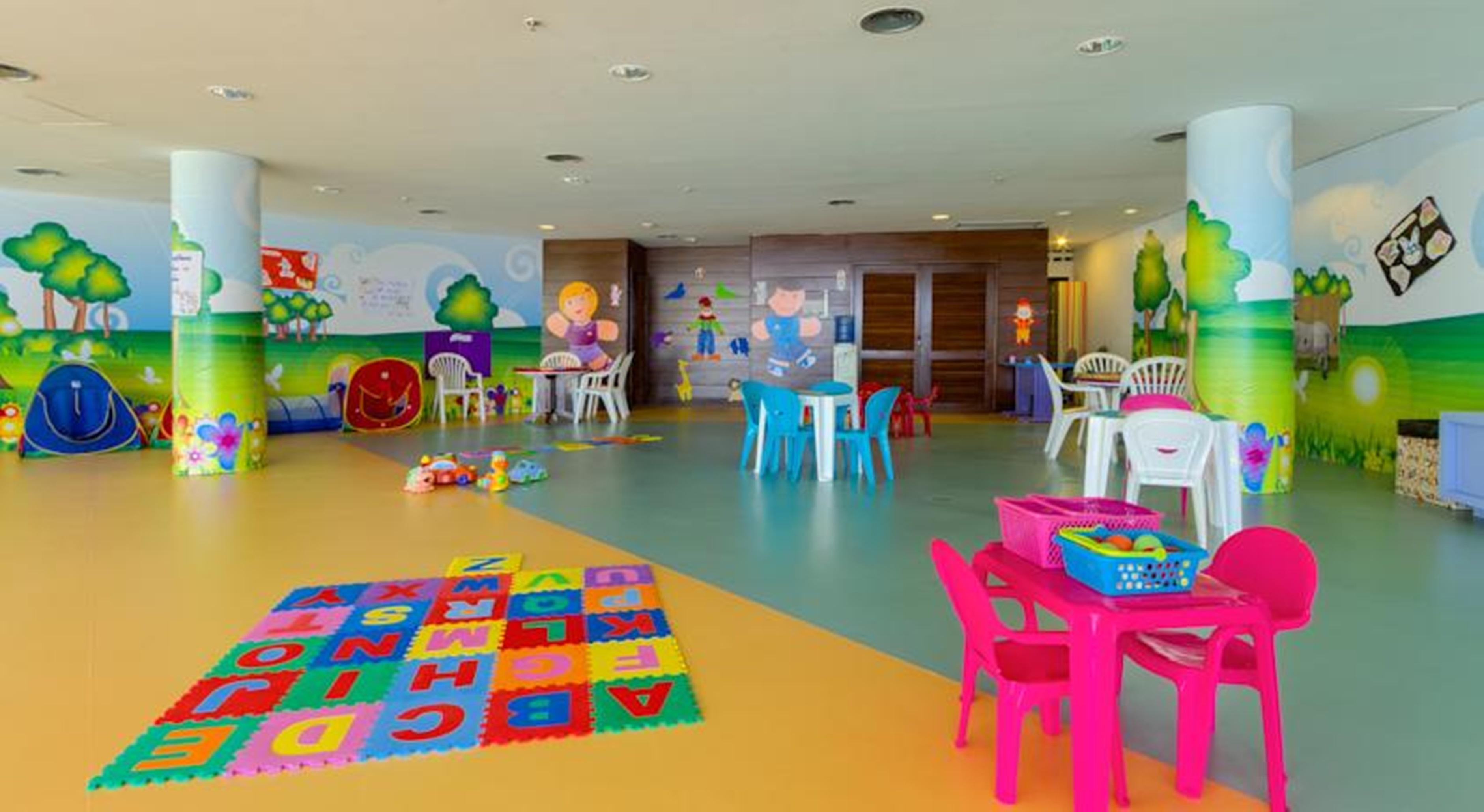 Hotel Royal Tulip Brasilia Alvorada Exterior foto The photo shows a colorful and spacious children's playroom. The floor is divided into sections with different colors, and there is a large play mat featuring letters and numbers. 

In the room, there are several small, lightweight tables and chairs 
